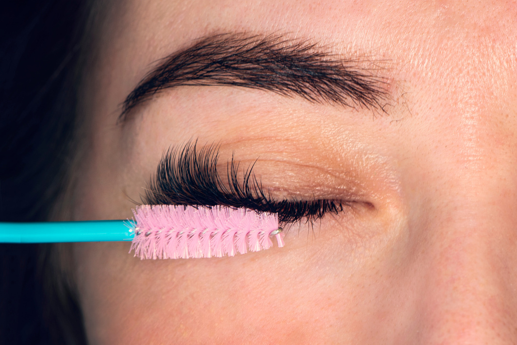 combing the extended eyelashes. Woman eye with beautiful makeup and long eyelashes. Mascara Brush. Eyelash Care Treatment: eyelash lifting, staining, curling, laminating and extension for lashes.